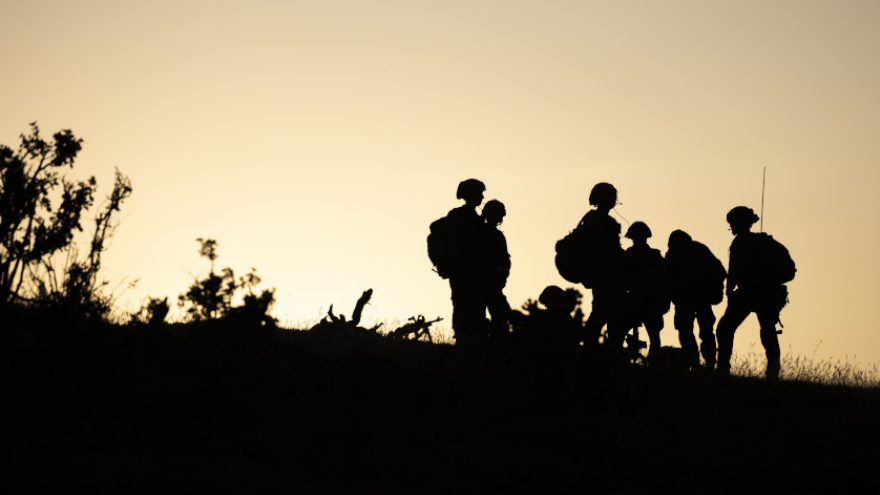 A group of silhouetted soldiers stand on a hill at sunset.