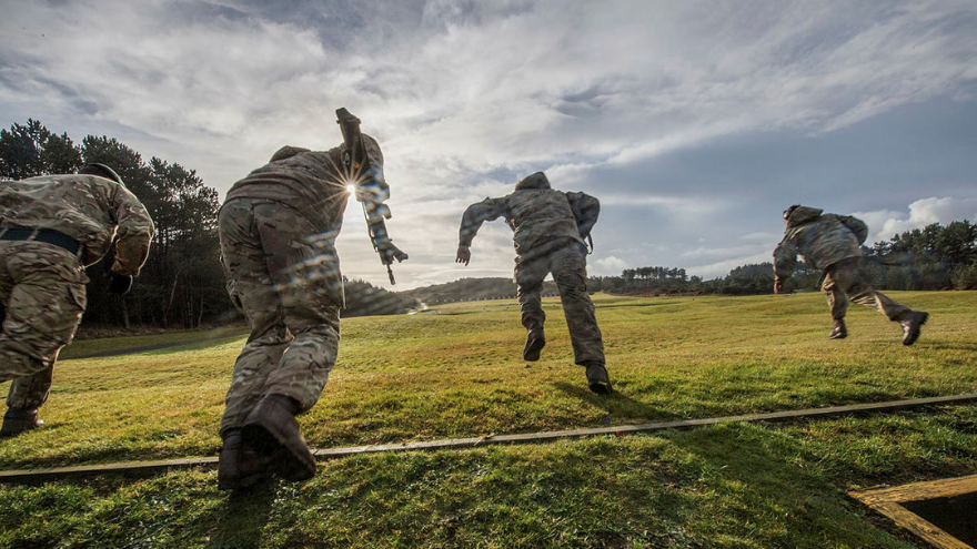 Soldiers in camouflage run uphill on a grassy field