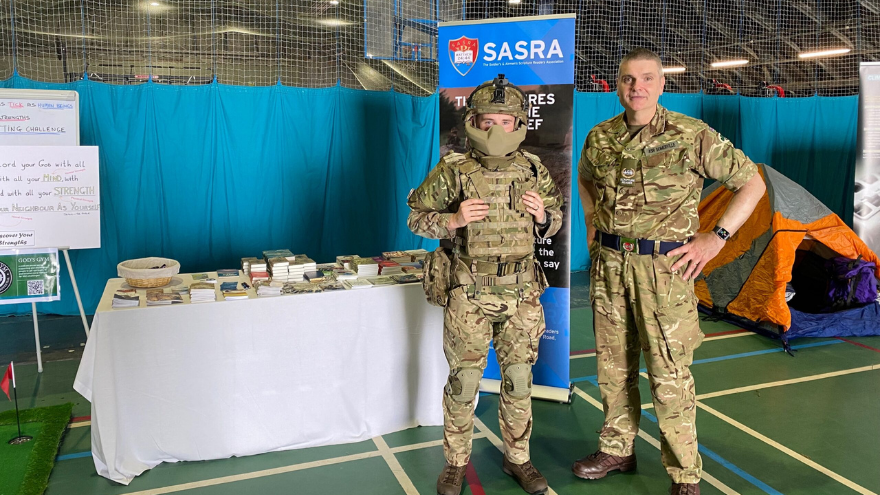 ASR Paul Somerville stands with another soldier in front of a stand at a Health Fair