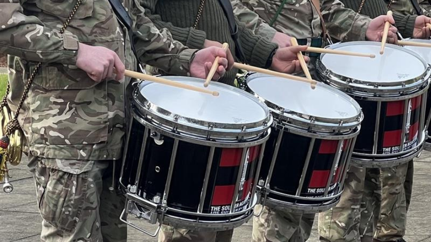 A row of soldiers in uniform playing snare drums