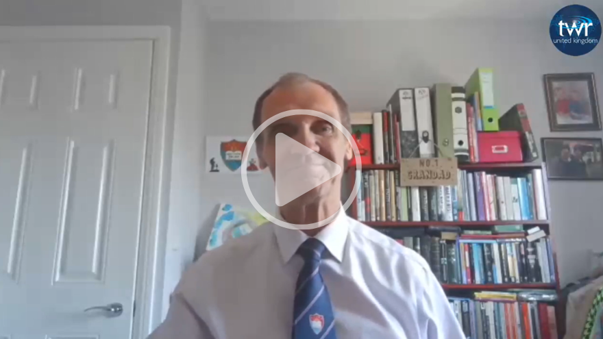 Executive Director Matin Gliniecki wearing a shirt and tie sits in a home office with bookshelves, folders, and framed pictures in the background. With the TWR logo in the top right corner and a play button in the middle of the screen.